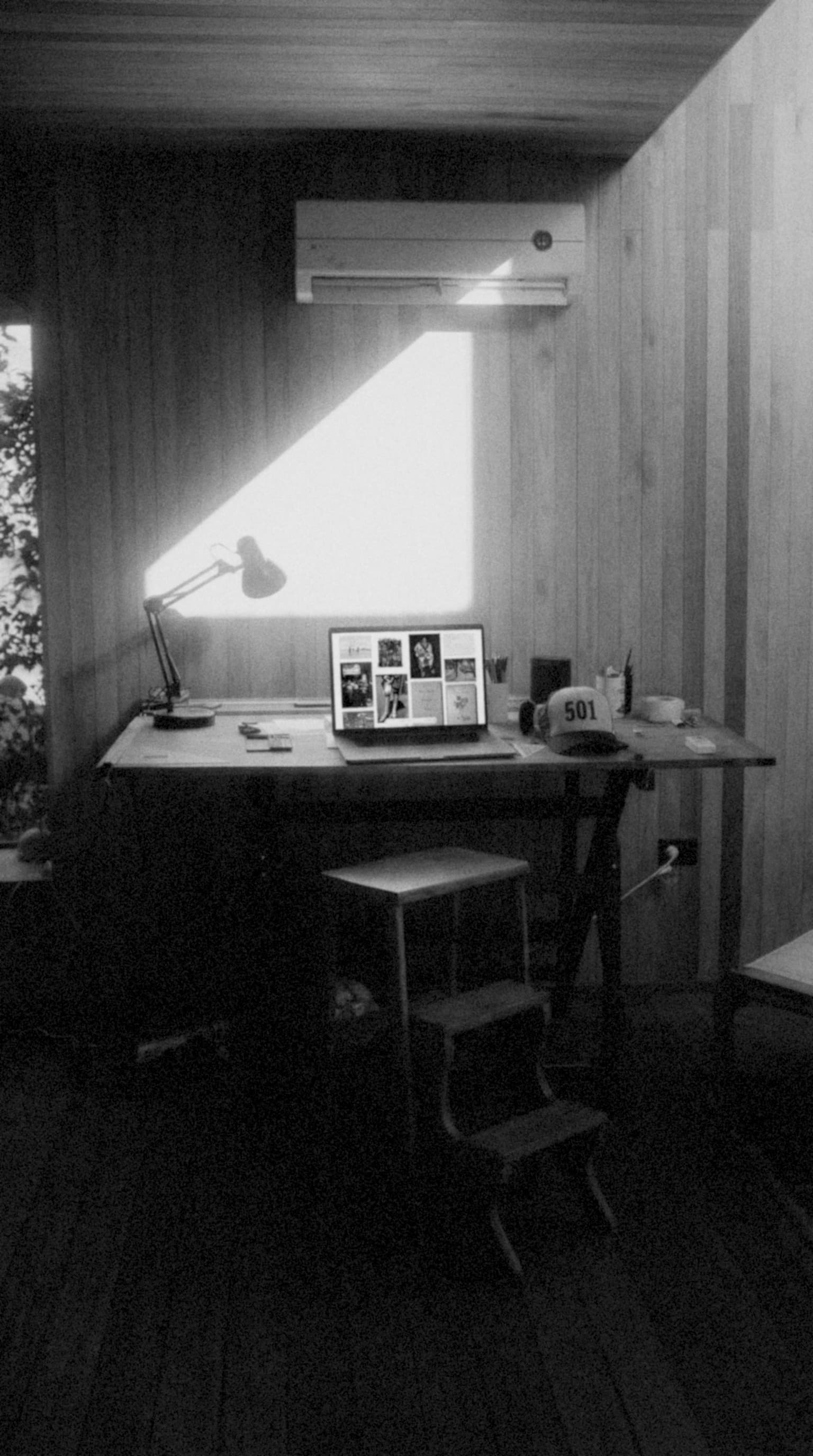 A quiet wooden desk with a laptop and angled sunlight.